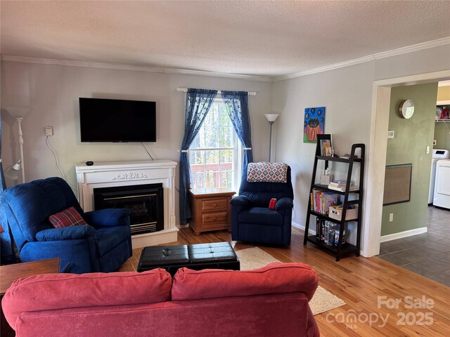 living area with ornamental molding, a glass covered fireplace, wood finished floors, washer / clothes dryer, and a textured ceiling