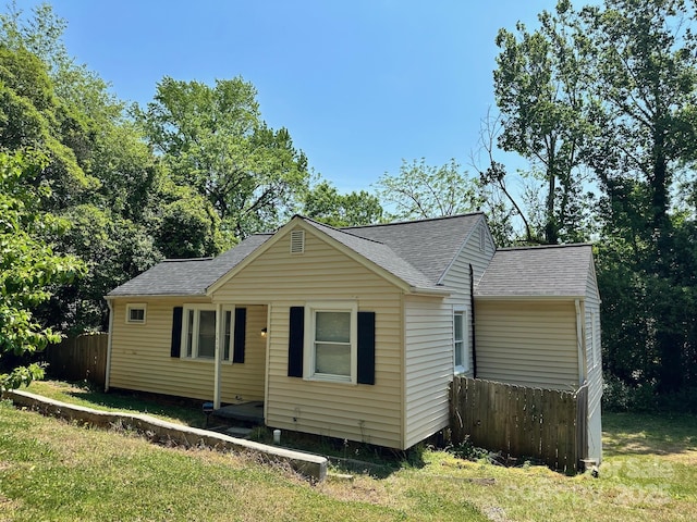 view of front of home with a front lawn, roof with shingles, and fence