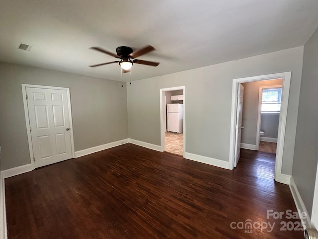unfurnished bedroom featuring a ceiling fan, visible vents, baseboards, freestanding refrigerator, and dark wood-style floors