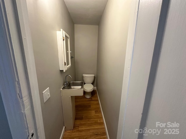 half bath featuring a sink, baseboards, toilet, and wood finished floors