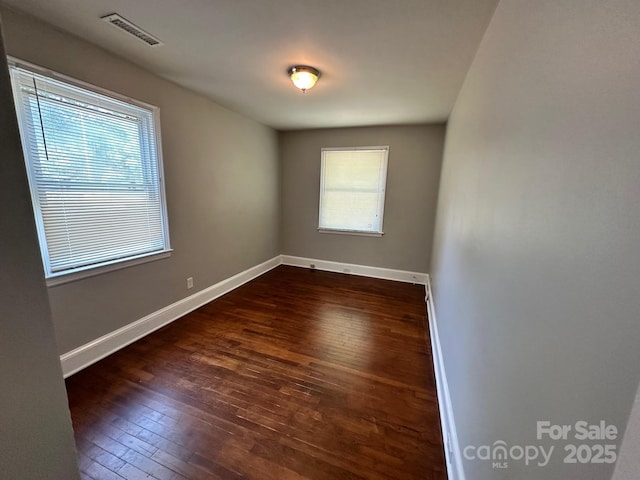 empty room featuring baseboards, visible vents, and dark wood-type flooring
