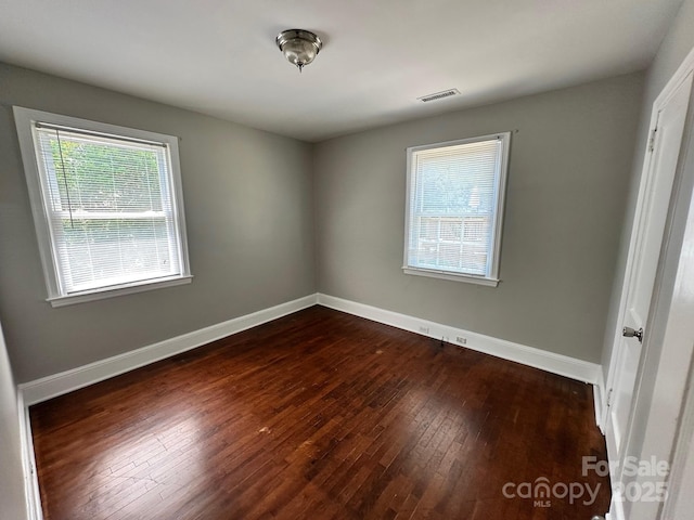 empty room featuring baseboards, dark wood-style floors, and visible vents