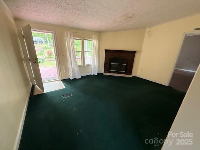 unfurnished living room featuring a fireplace with raised hearth, dark colored carpet, a textured ceiling, and visible vents