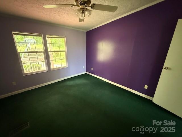 spare room featuring crown molding, baseboards, dark carpet, ceiling fan, and a textured ceiling