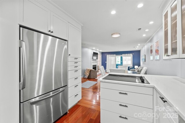 kitchen with wood-type flooring, freestanding refrigerator, glass insert cabinets, open floor plan, and black electric stovetop