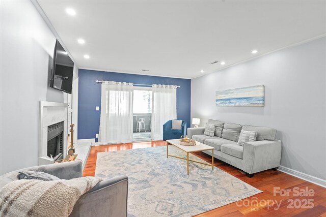 living area with a fireplace with raised hearth, baseboards, recessed lighting, and wood finished floors