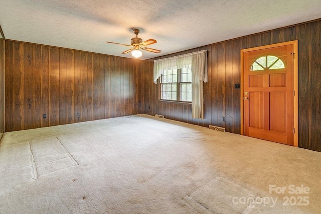 entrance foyer featuring a ceiling fan, wood walls, a textured ceiling, and carpet floors