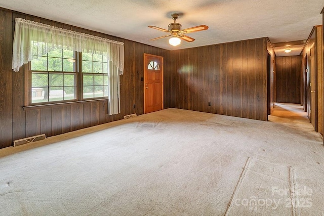 carpeted entrance foyer featuring a ceiling fan, a textured ceiling, and wooden walls