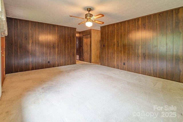 spare room with wooden walls, a ceiling fan, and carpet flooring