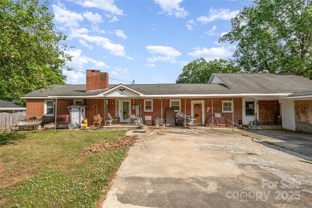 ranch-style house featuring covered porch, brick siding, driveway, and a chimney