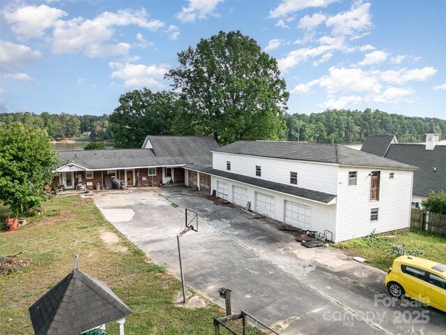 back of property with a garage, fence, roof with shingles, concrete driveway, and a porch
