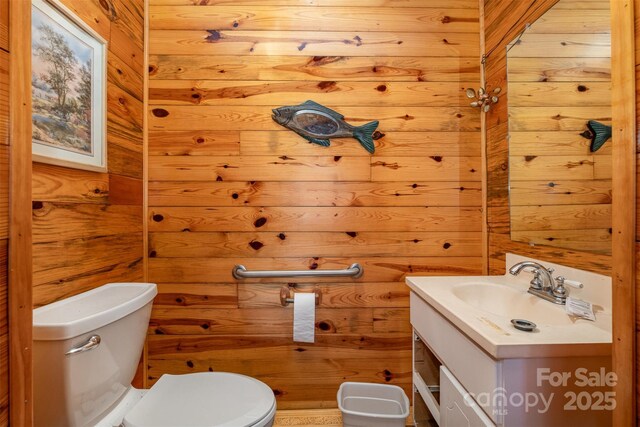 half bath with wooden walls, vanity, and toilet