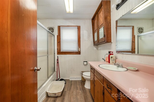 bathroom featuring vanity, toilet, tile walls, wood finished floors, and bath / shower combo with glass door