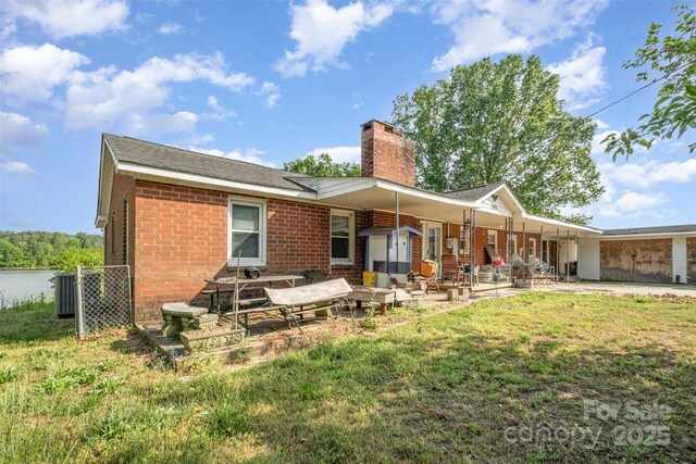 rear view of house featuring brick siding, a chimney, cooling unit, a patio, and a yard