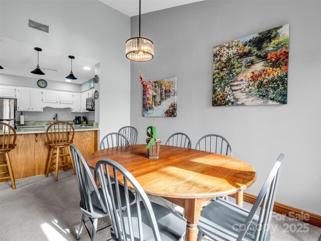 dining area featuring a chandelier, light colored carpet, visible vents, and baseboards