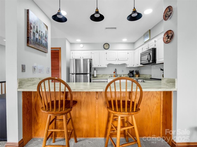 kitchen with visible vents, black microwave, light countertops, freestanding refrigerator, and a peninsula