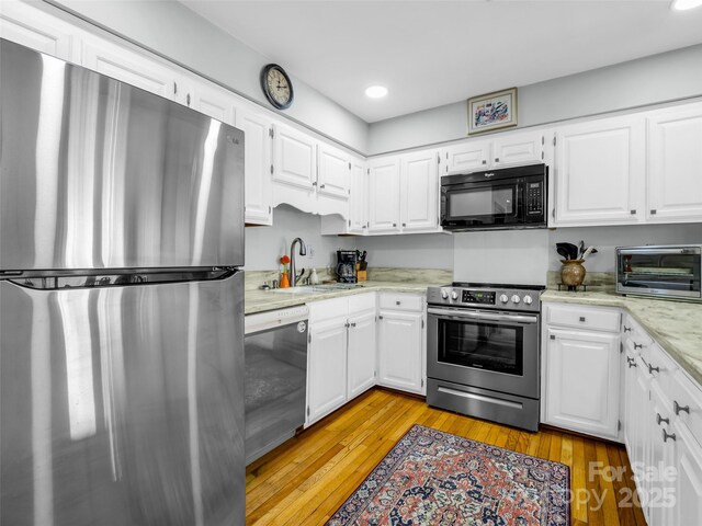 kitchen with appliances with stainless steel finishes, light wood-type flooring, a sink, a toaster, and white cabinets