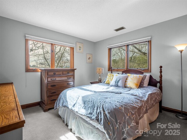 bedroom featuring light colored carpet, a textured ceiling, baseboards, and visible vents