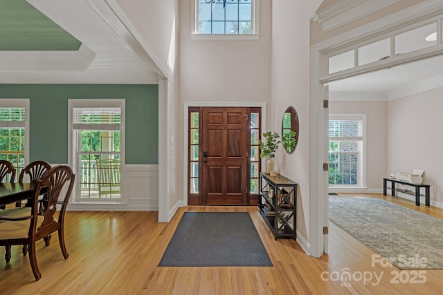 entryway with crown molding, light wood-style flooring, a wainscoted wall, and a healthy amount of sunlight