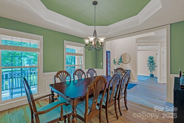 dining area with crown molding, wainscoting, a raised ceiling, a chandelier, and light wood-type flooring