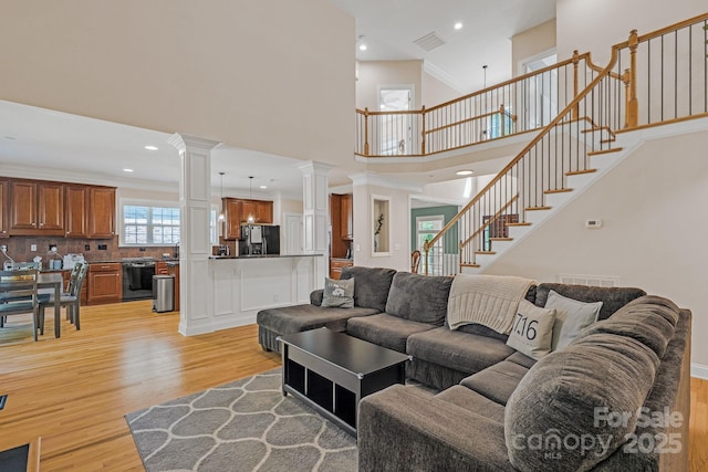 living area featuring visible vents, light wood-type flooring, stairs, a high ceiling, and ornate columns