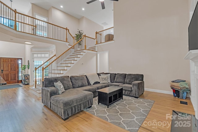 living room featuring stairs, a towering ceiling, wood finished floors, baseboards, and a ceiling fan