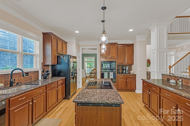 kitchen featuring a sink, black appliances, light wood finished floors, and an island with sink