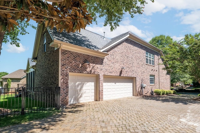 view of home's exterior featuring brick siding, decorative driveway, roof with shingles, and fence