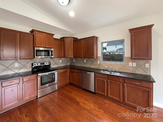 kitchen with dark countertops, appliances with stainless steel finishes, a sink, dark wood-type flooring, and vaulted ceiling