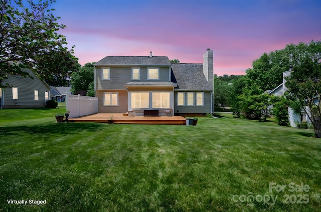 back of house at dusk with a lawn, a wooden deck, and a chimney