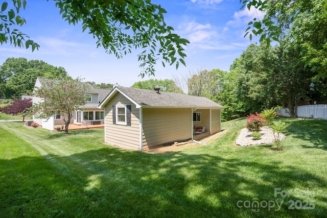 rear view of property featuring a yard, fence, and a shingled roof