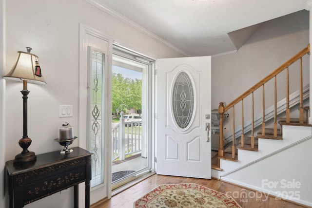 entrance foyer with ornamental molding, wood finished floors, and stairway