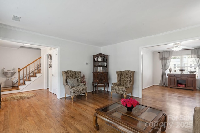 living room with light wood-style floors, stairs, a ceiling fan, baseboards, and ornamental molding