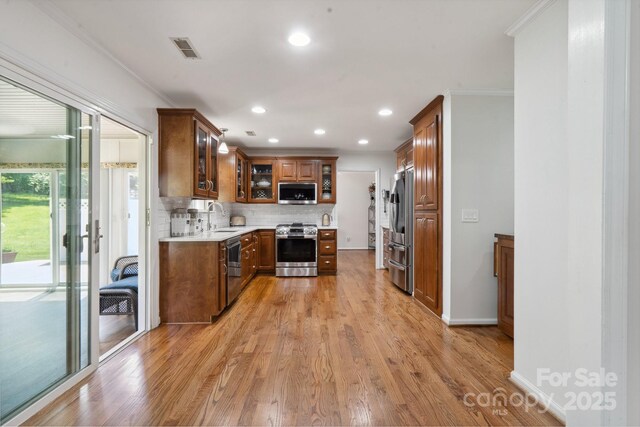 kitchen with decorative backsplash, brown cabinets, a sink, light wood finished floors, and stainless steel appliances