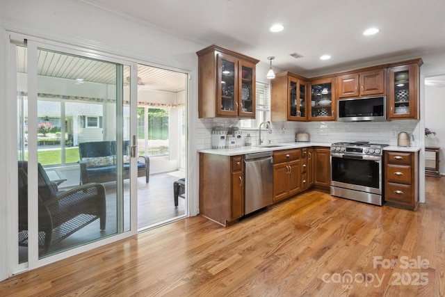 kitchen with decorative backsplash, light wood-type flooring, a sink, light countertops, and stainless steel appliances