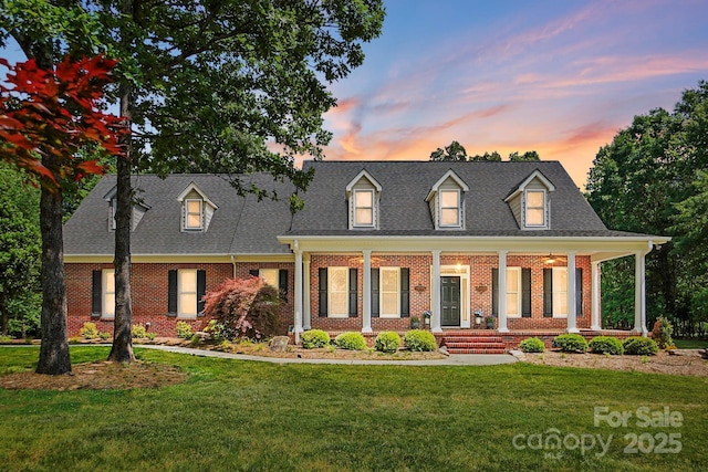 view of front of house with a porch, a lawn, roof with shingles, and brick siding