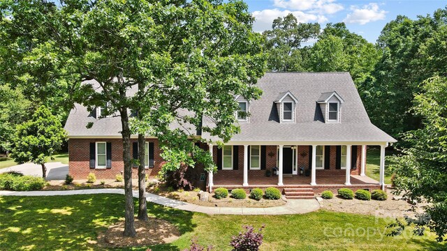 cape cod-style house with covered porch, brick siding, and a front lawn