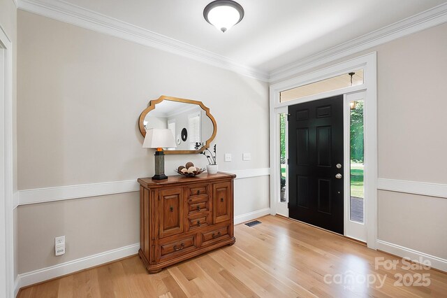 foyer with baseboards, ornamental molding, light wood finished floors, and visible vents