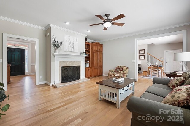 living room featuring light wood-style floors, ceiling fan, stairway, and crown molding