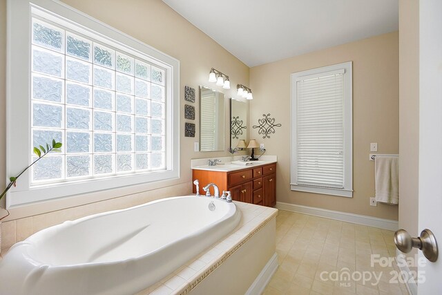 full bathroom featuring a healthy amount of sunlight, baseboards, double vanity, and a bath