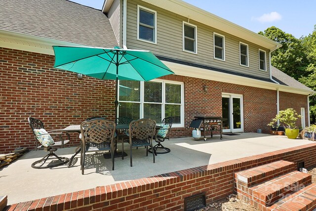 rear view of property with brick siding, a shingled roof, and a patio area