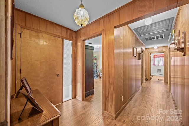 corridor with visible vents, light wood finished floors, wooden walls, and baseboard heating
