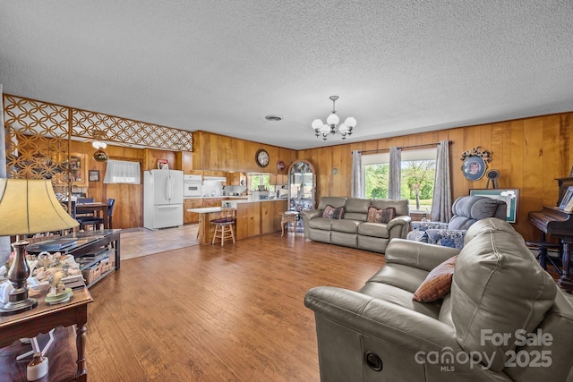 living room with light wood-style floors, wood walls, a textured ceiling, and a notable chandelier