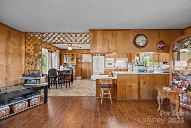 kitchen with brown cabinetry, a peninsula, white appliances, light countertops, and a textured ceiling