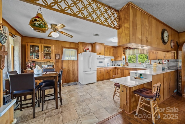kitchen with wooden walls, crown molding, white appliances, a textured ceiling, and a peninsula