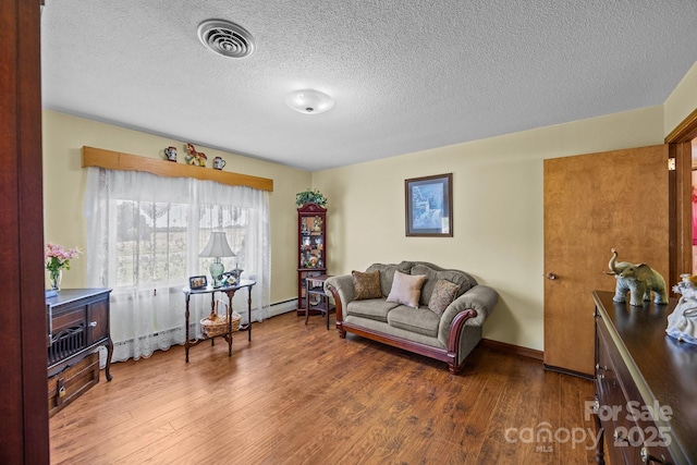 living room with visible vents, baseboards, a textured ceiling, and wood finished floors