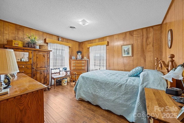 bedroom featuring wooden walls, a textured ceiling, wood finished floors, and visible vents