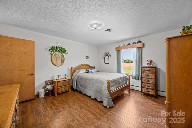 bedroom featuring a textured ceiling, baseboard heating, wood finished floors, and visible vents