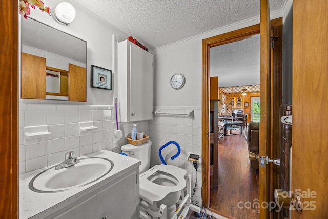 bathroom with a textured ceiling, tile walls, a wainscoted wall, vanity, and toilet