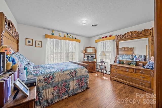 bedroom featuring a textured ceiling, baseboard heating, hardwood / wood-style floors, and visible vents